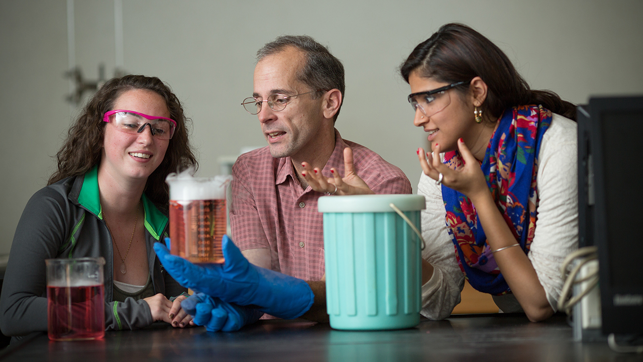 Male faculty and two female students examining chemicals