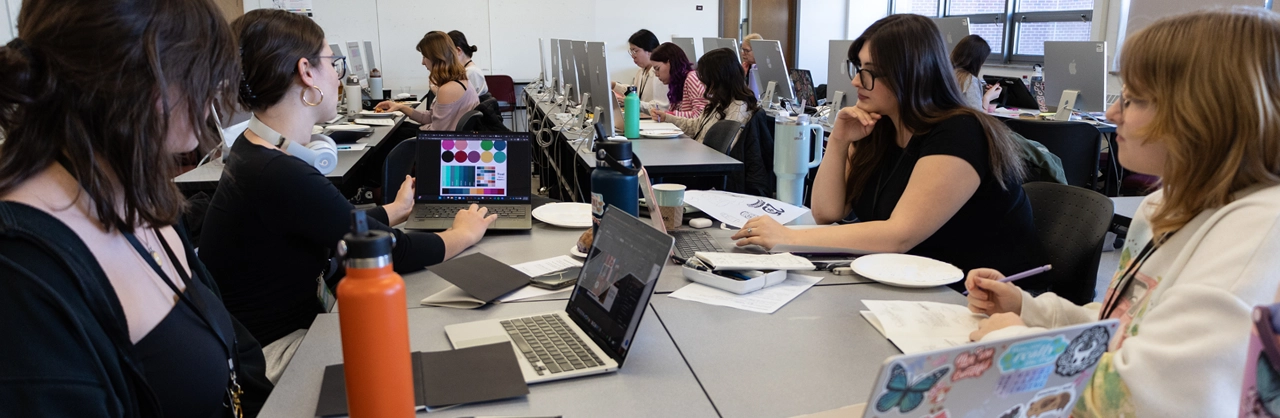 A group of female students gathered around a table with laptops working on a project together