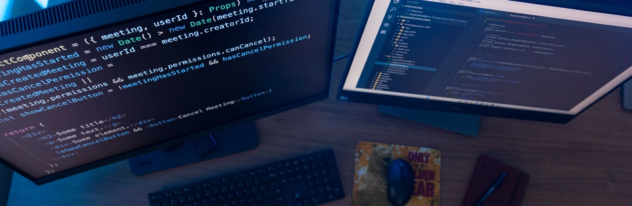 two computer monitors on a desk with software development code on the screens