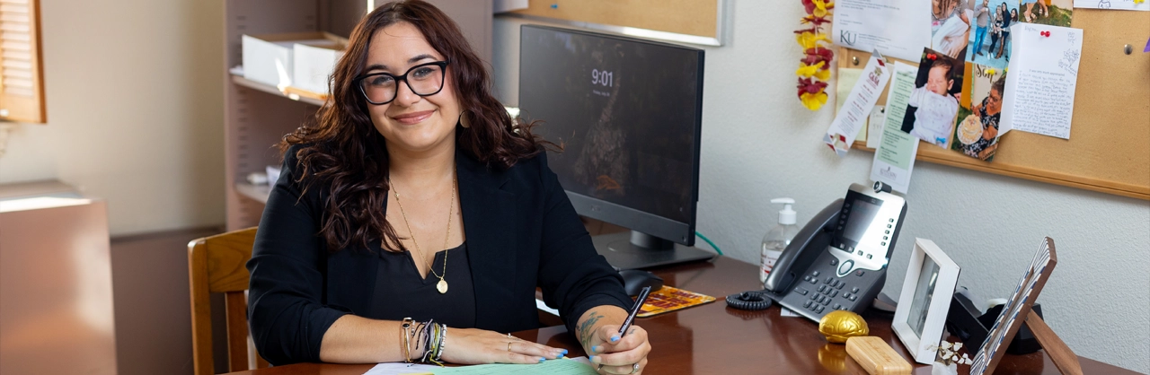 A woman siting at a desk with a pen in her hand writing on paper