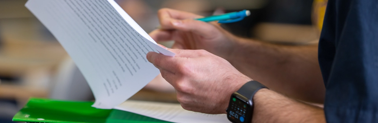 Hands lifting a paper back with one hand and a pencil in the other about to write on the paper