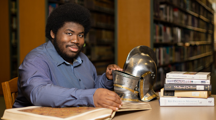 Male student sitting at desk in library with historical artifacts from his history degree at Kutztown University.