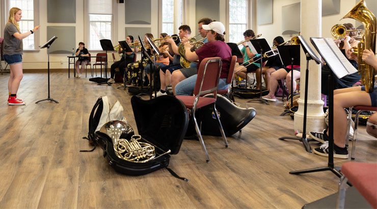 a class of musicians holding instruments with a female student in front teaching and leading them