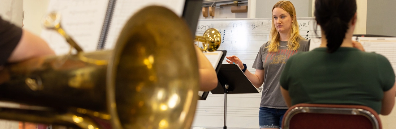 a female student standing in front of class with instruments teaching