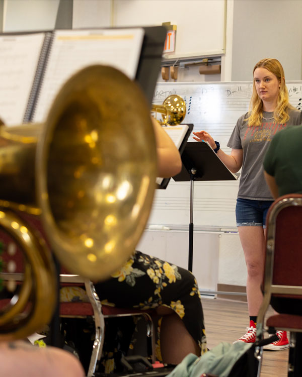a female student standing in front of class with instruments teaching