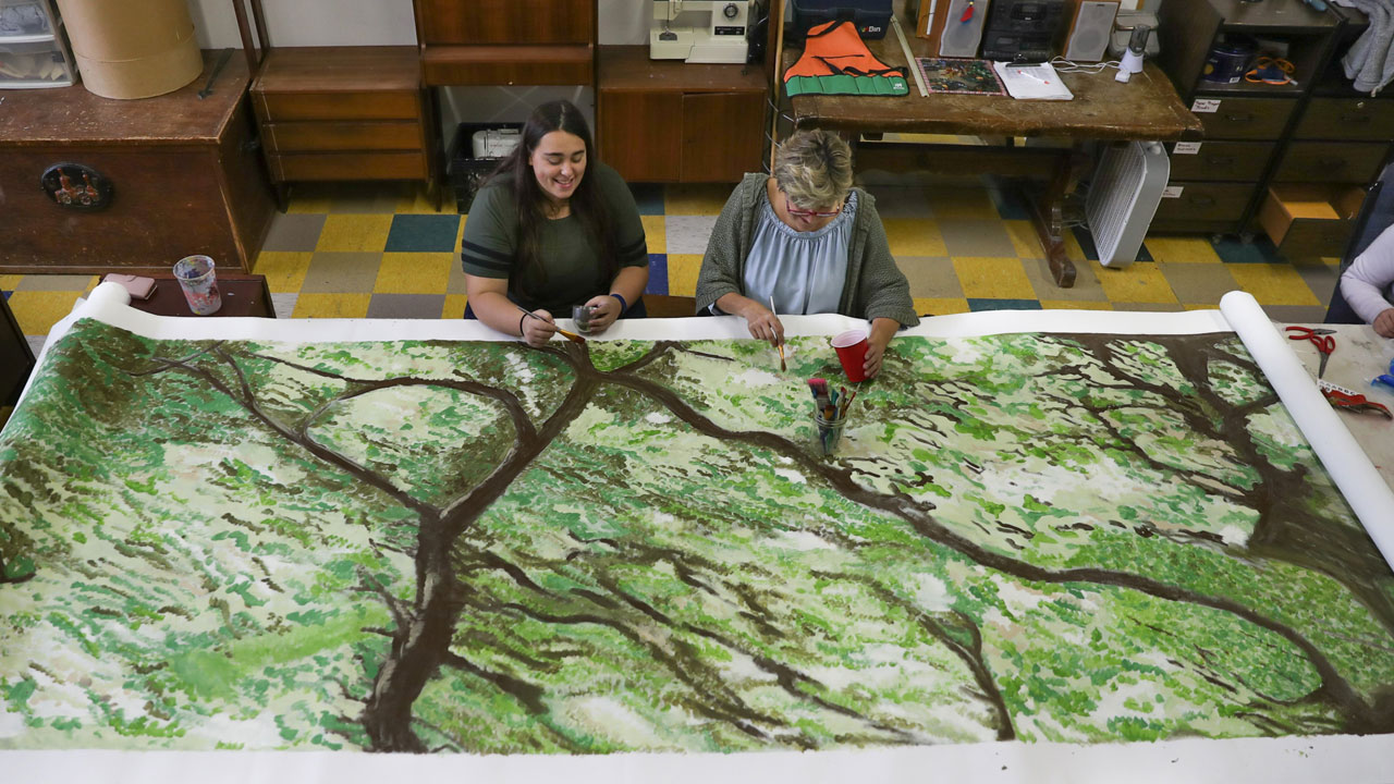 two artists paiting a large canvas of a nature scene.
