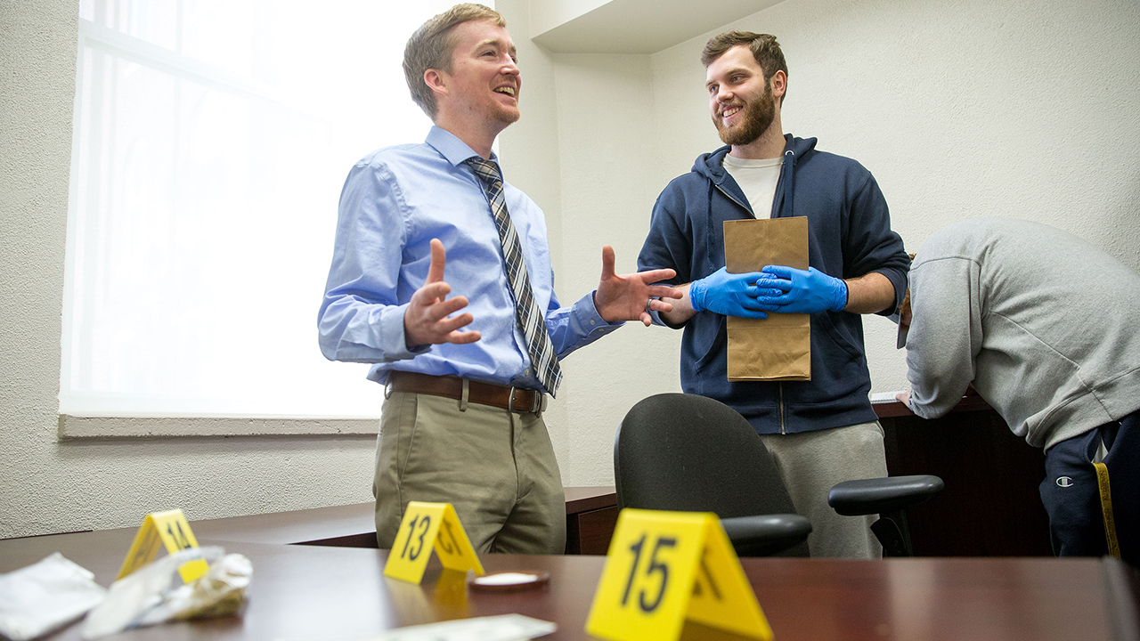 two students talking holding evidence bag at mock crime scene