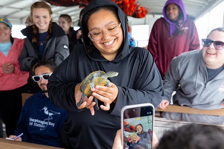female student in front of several other students, holding a turtle.