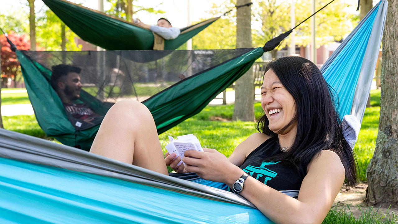 three students lying in hammocks outside of Rohrbach Library, studying flashcards and laughing.