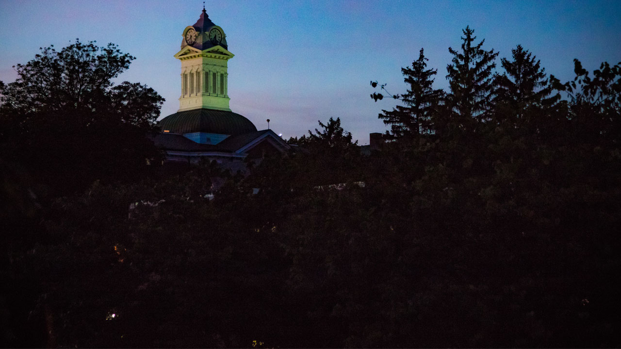 Far shot of the Old Main clock tower with trees in the foreground
