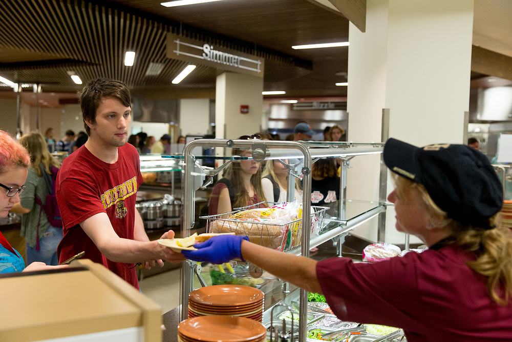dining worker serving food to students in cafeteria setting.