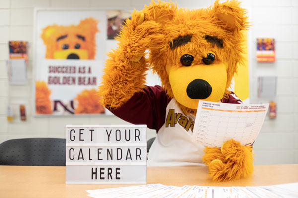 Avalanche Golden Bear, holding CASA calendar "Get your calendar here" appears on sign in foreground.